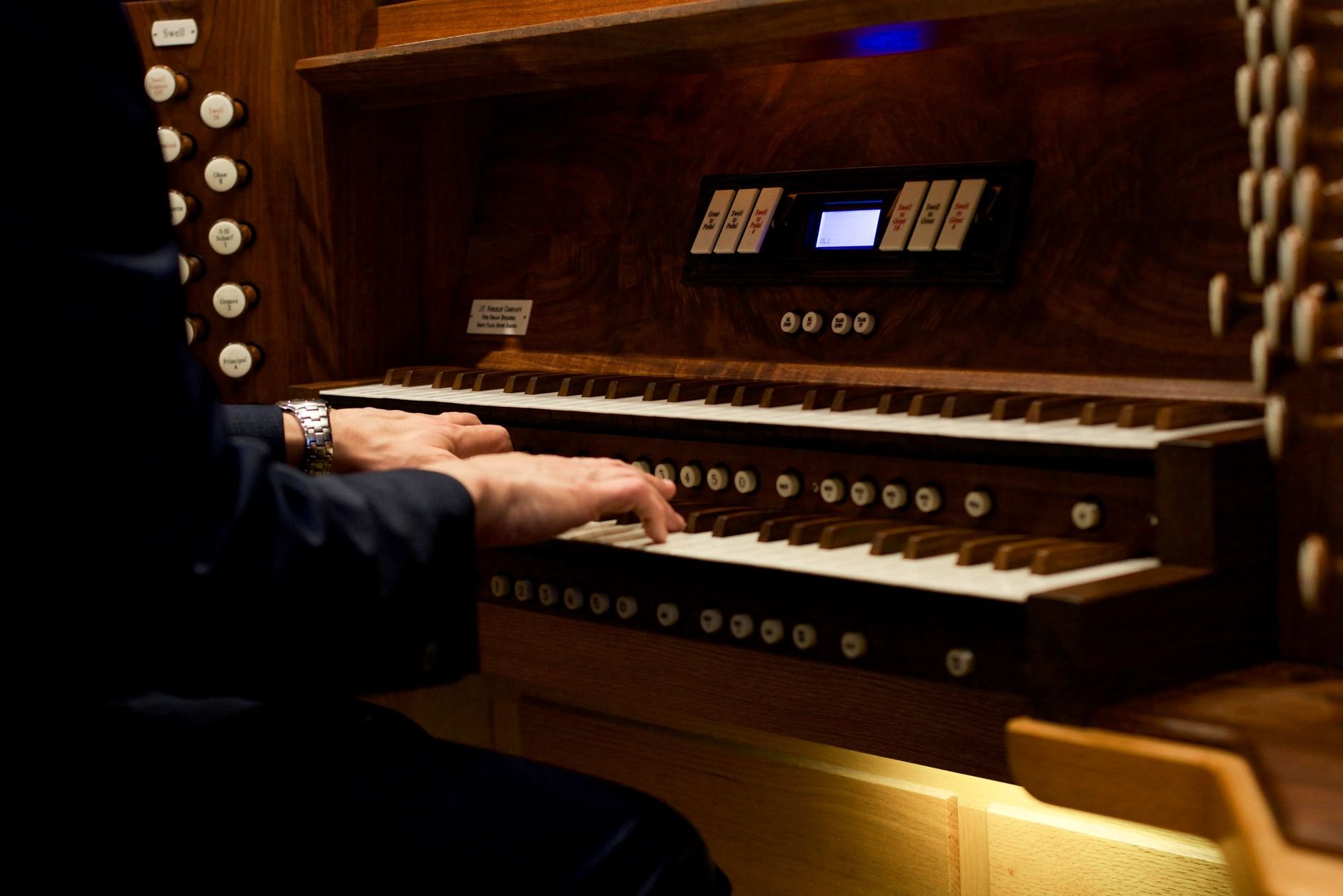 Close-up of a musician's hands playing an ornate church organ keyboard.
