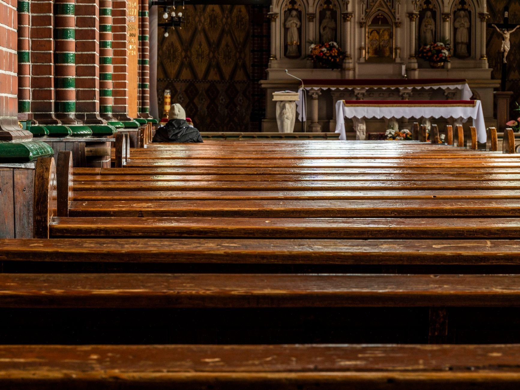 Empty church interior with wooden pews leading to richly decorated altar, warm atmosphere.